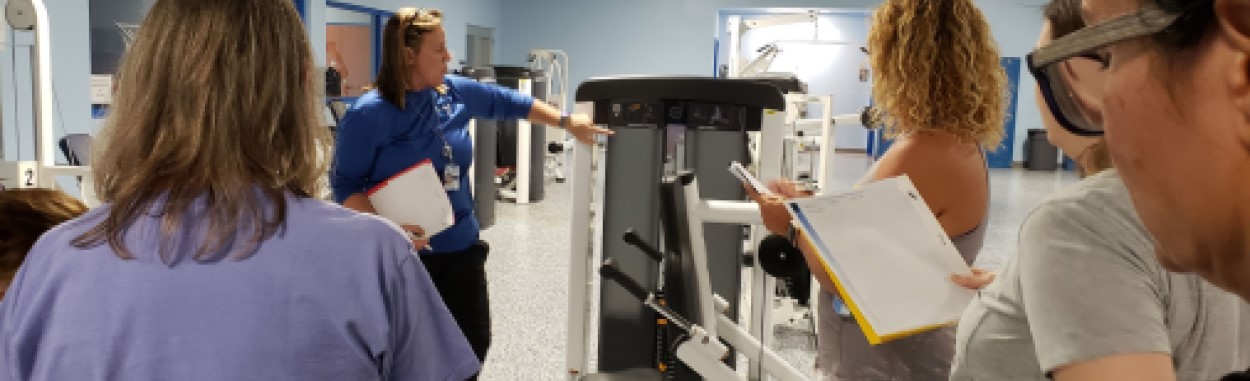 exercise trainer explaining how to use an exercise machine to participants